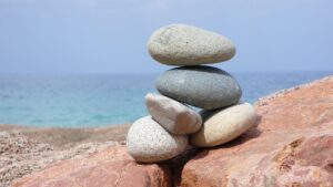 A small pile of 5 stones resting on two large boulders with a sea sky horizon background